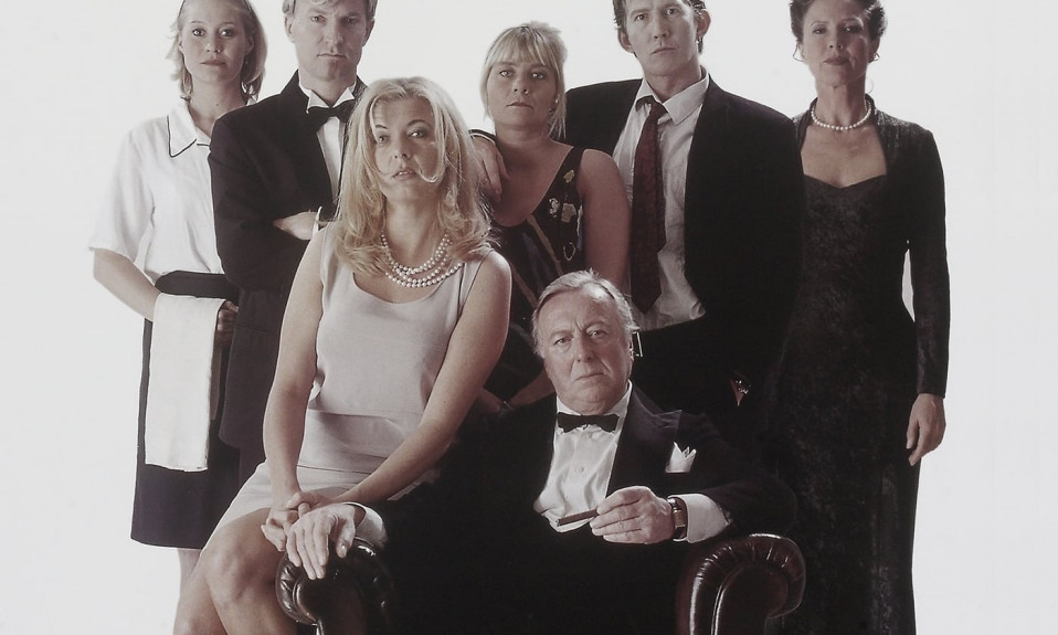 A movie poster shows a white family with emotionless expressions dressed in black-tie attire posing for a photo. There are seven adults, six of whom are posed around an old man in an armchair at the from. The background is plain white and the title of the film, "FESTEN", is printed at the top.